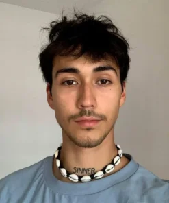 Hombre con Collar de Conchas Hombre; cuero trenzado y cauri, estilo surfer, luz natural.