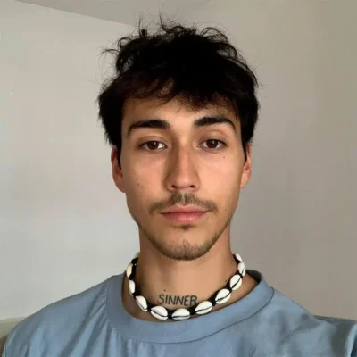 Hombre con Collar de Conchas Hombre; cuero trenzado y cauri, estilo surfer, luz natural.