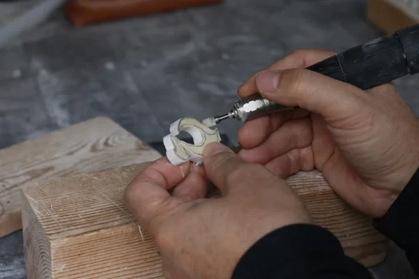 Artesano tallando a mano colgante Hei Matau en hueso natural, símbolo maorí de protección y fuerza